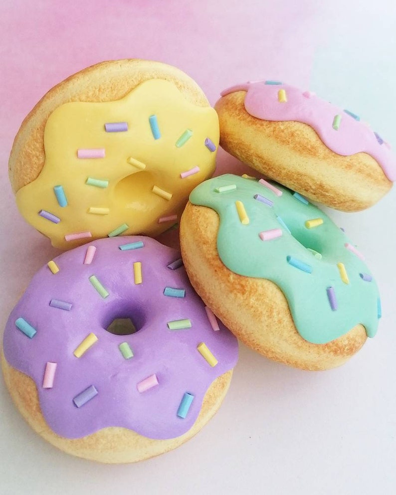 May include: Four mini donuts with different colored frosting and sprinkles. The donuts are yellow, pink, green, and purple.