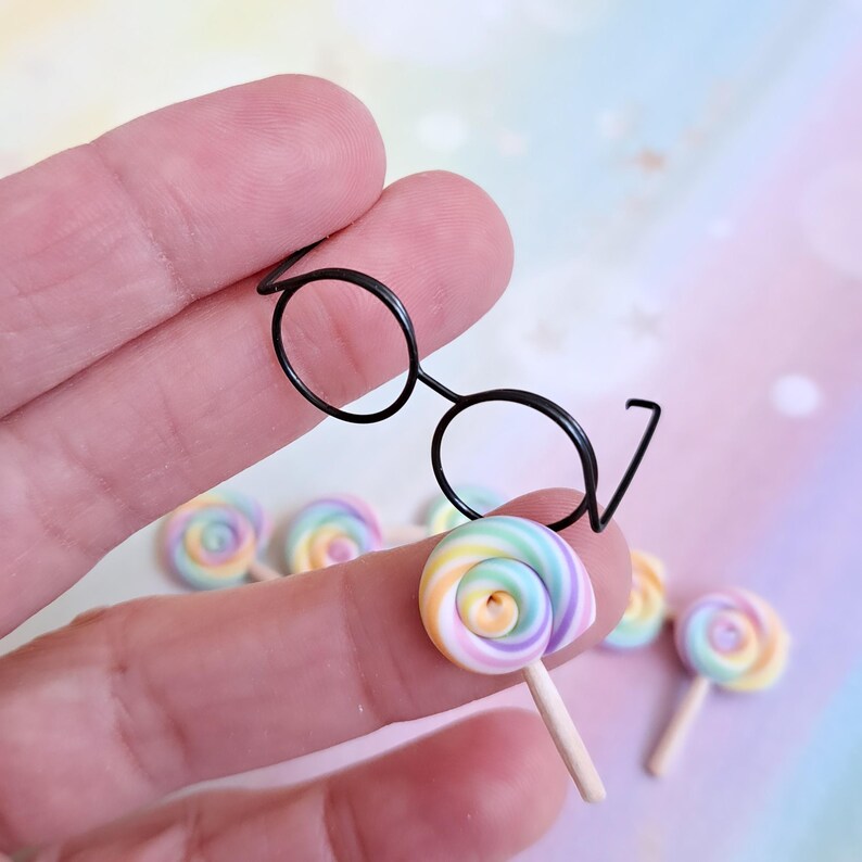 May include: A set of miniature rainbow swirl lollipops with black wire-rimmed glasses. The lollipops are on sticks and are made of polymer clay.