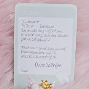 May include: A rectangular white card with rounded corners featuring German text that reads: "Lieber Gl&uuml;ckwunsch! Zu Deiner Zahnl&uuml;cke. Ich bin sehr stolz auf Dich und freu mich riesig, dass dein Wackelzahn so toll geputzt ist. Mach weiter so und pass gut auf Deinen neuen Zahn auf. Es bedankt sich ganz herzlich... Deine Zahnfee Datum:".