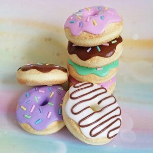 May include: A stack of six colorful donuts with various toppings, including chocolate, sprinkles, and frosting. The donuts are arranged in a pyramid shape, with the largest donut on the bottom and the smallest donut on top.