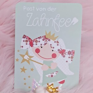 May include: A rectangular light green card featuring the text Post von der Zahnfee and a graphic of a fairy with a gold crown, pink cheeks, and a star-tipped wand. The fairy has hair decorated with red and white star patterns and wears a green dress.
