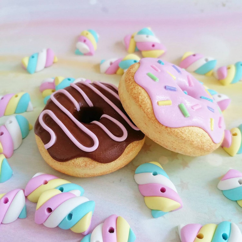 May include: Two colorful donuts with different toppings. One donut is topped with pink frosting and colorful sprinkles, the other with chocolate frosting and pink stripes. The donuts are surrounded by colorful candy.