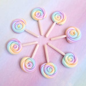 May include: Eight rainbow swirl lollipops on wooden sticks arranged in a circle on a pink and purple ombre background.