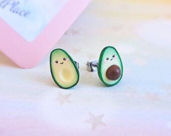 Könnte beinhalten: Ein Paar Avocado-Ohrringe mit einem süßen lächelnden Gesicht. Die Ohrringe sind aus grünem und braunem Polymerton gefertigt und haben silberne Ohrstecker.