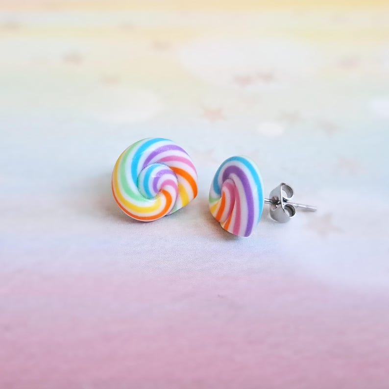 K&ouml;nnte beinhalten: Ein Paar Regenbogen-Wirbel-Ohrstecker mit silbernen Stiften. Die Ohrringe sind aus Polymer Clay gefertigt und haben einen wei&szlig;en Hintergrund mit bunten Streifen.