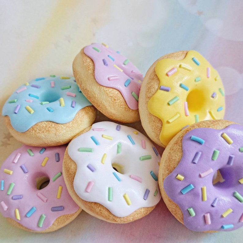 May include: Six pastel-colored donuts with colorful sprinkles. The donuts are arranged in a circle with the yellow donut at the top.
