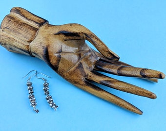 May include: A pair of silver dangle earrings with multiple small round beads. The earrings are hanging from a wooden hand.