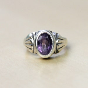 May include: A silver ring with an oval-shaped amethyst gemstone set in a decorative band.