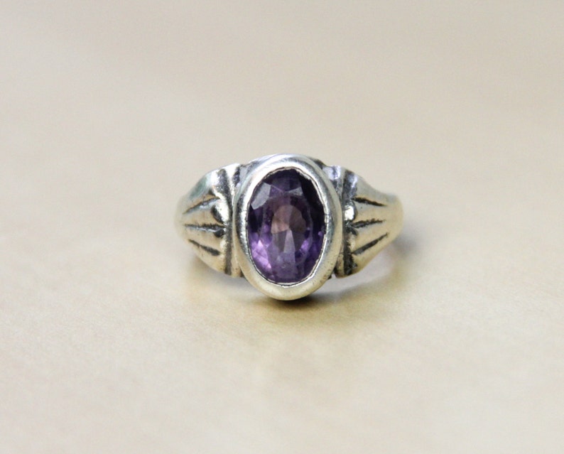 May include: A silver ring with an oval-shaped amethyst gemstone set in a decorative band.