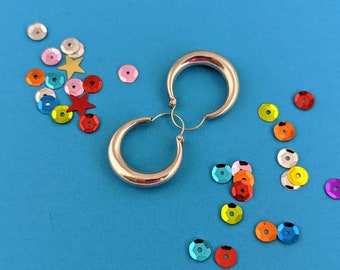 May include: A pair of silver hoop earrings on a blue background with colorful sequins scattered around them.