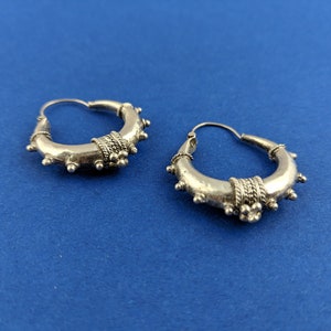 May include: A pair of silver hoop earrings with a textured design. The earrings have a circular shape and are decorated with small, raised dots and a band of intricate detail.