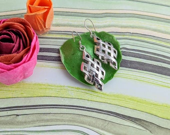 May include: A pair of silver earrings with a knot design. The earrings are on a green background.