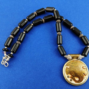 May include: A black onyx beaded necklace with a silver clasp and a round pendant featuring an etched gold elephant design.