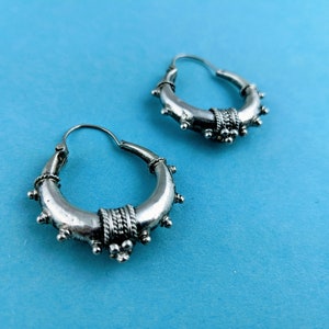 May include: A pair of silver hoop earrings with a decorative design. The earrings have a circular shape and are adorned with small beads and a textured band.