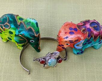 Puede incluir: Dos figuritas de elefante de madera pintadas de colores vivos con una pulsera de plata con una piedra turquesa y piedras rojas.