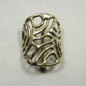 May include: A gold-colored hair barrette with an open, organic design. The barrette is rectangular with a curved top and bottom, featuring a series of interconnected, flowing lines. The clasp is a simple, rounded post.