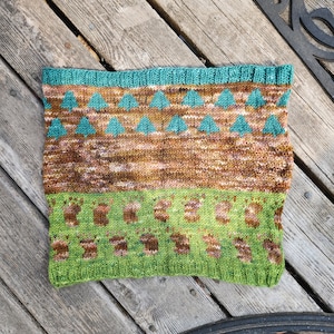 May include: A knitted green and brown scarf with a pattern of trees and a border of teal triangles.