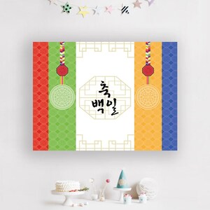 May include: A white banner with a gold frame and a traditional Korean design. The banner has a red, green, yellow, and blue background with a gold octagon in the center. The octagon contains the Korean characters "축  백일" which translates to "Happy 100th Day".
