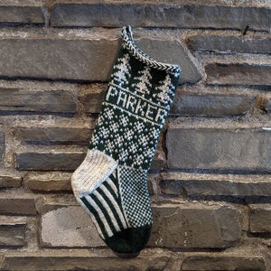Christmas stocking knit with green and white yarn hangs on a grey stone wall