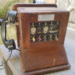 May include: A vintage wooden rotary phone with a black handset and a metal plaque that reads "PROPRIETE DE L'ETAT MARCHE DU 8 AVRIL 1953 TABLEAU POUR RESEAU OU AUTO RURAL CH. MILDE 60 R. Dewenaudes Paris".