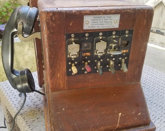 Pode incluir: Um telefone rotativo de madeira vintage com um auricular preto e uma placa de metal que diz "PROPRIETE DE L'ETAT MARCHE DU 8 AVRIL 1953 TABLEAU POUR RESEAU OU AUTO RURAL CH. MILDE 60 R. Dewenaudes Paris".