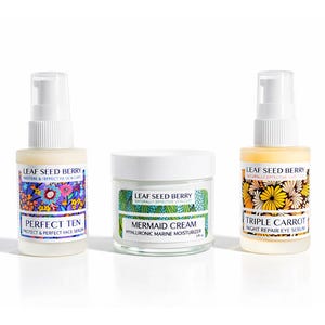 May include: Three Leaf Seed Berry skincare products: a Perfect Ten face serum, Mermaid Cream hyaluronic moisturizer, and Triple Carrot night repair eye serum. Each product is in a clear bottle or jar with a white lid and colorful floral labels.