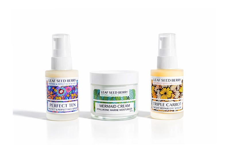 May include: Three Leaf Seed Berry skincare products: a Perfect Ten face serum, Mermaid Cream hyaluronic moisturizer, and Triple Carrot night repair eye serum. Each product is in a clear bottle or jar with a white lid and colorful floral labels.