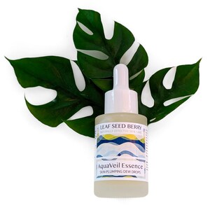 May include: A clear glass bottle of AquaVeil Essence skin-plumping dew drops with a white dropper top. The bottle is labeled with the text "LEAF SEED BERRY" and "NATURALLY EFFECTIVE SKIN CARE". The bottle is set against a backdrop of large green leaves.