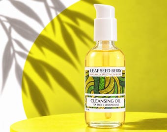 Może przedstawiać: Przezroczysta szklana butelka olejku oczyszczającego z białą pompką dozującą. Etykieta zawiera napis LEAF SEED BERRY NATURALLY EFFECTIVE SKIN CARE CLEANSING OIL TEA TREE + LEMONGRASS 2 fl. oz. Wzór w kolorze zielonym i żółtym.