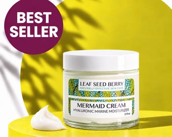May include: A clear glass jar of Leaf Seed Berry Mermaid Cream Hyaluronic Marine Moisturizer with a white lid. The label features green leaf patterns and text. A dollop of white cream sits beside the jar, which is labeled as 2 fl oz.