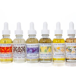 May include: Seven glass bottles with white dropper tops and labels. The labels are white with colorful illustrations and text. The text on the labels reads "Leaf Seed Berry Naturally Effective Skin Care" and the names of different essential oils: Ginger Turmeric, Frankincense, Lavender, Sweet Meadow, Chamomile, Vanilla Bean.
