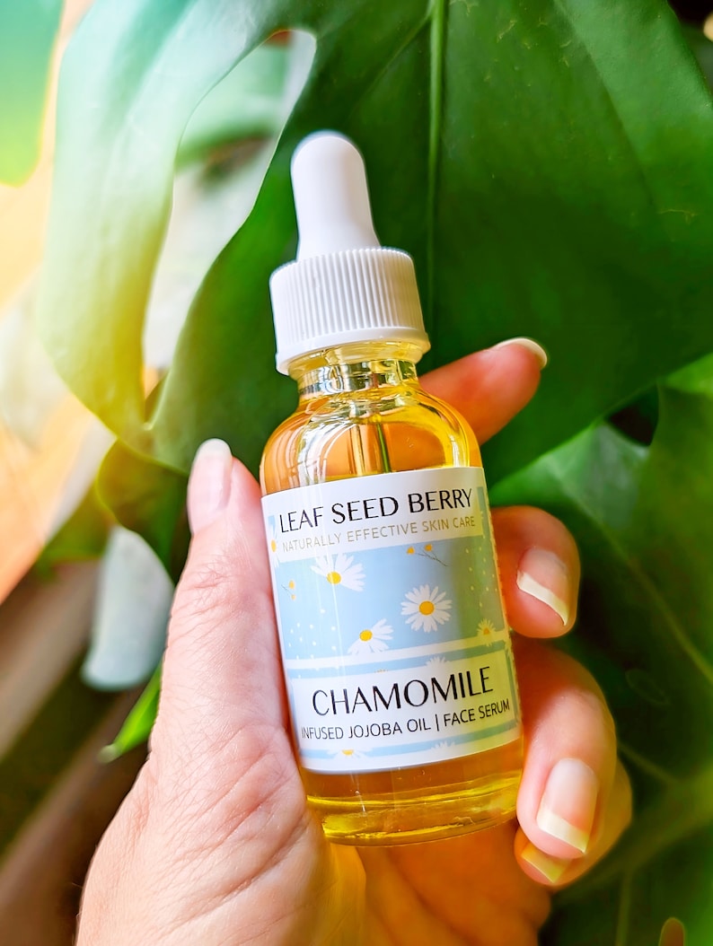 May include: A glass bottle of chamomile infused jojoba oil face serum. The bottle has a white dropper top and a label that says "Leaf Seed Berry Naturally Effective Skin Care" and "Chamomile Infused Jojoba Oil | Face Serum".