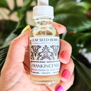 May include: A clear glass bottle with a white dropper top and a label that reads "Leaf Seed Berry Naturally Effective Skin Care Frankincense Infused Jojoba Oil | Face Serum"