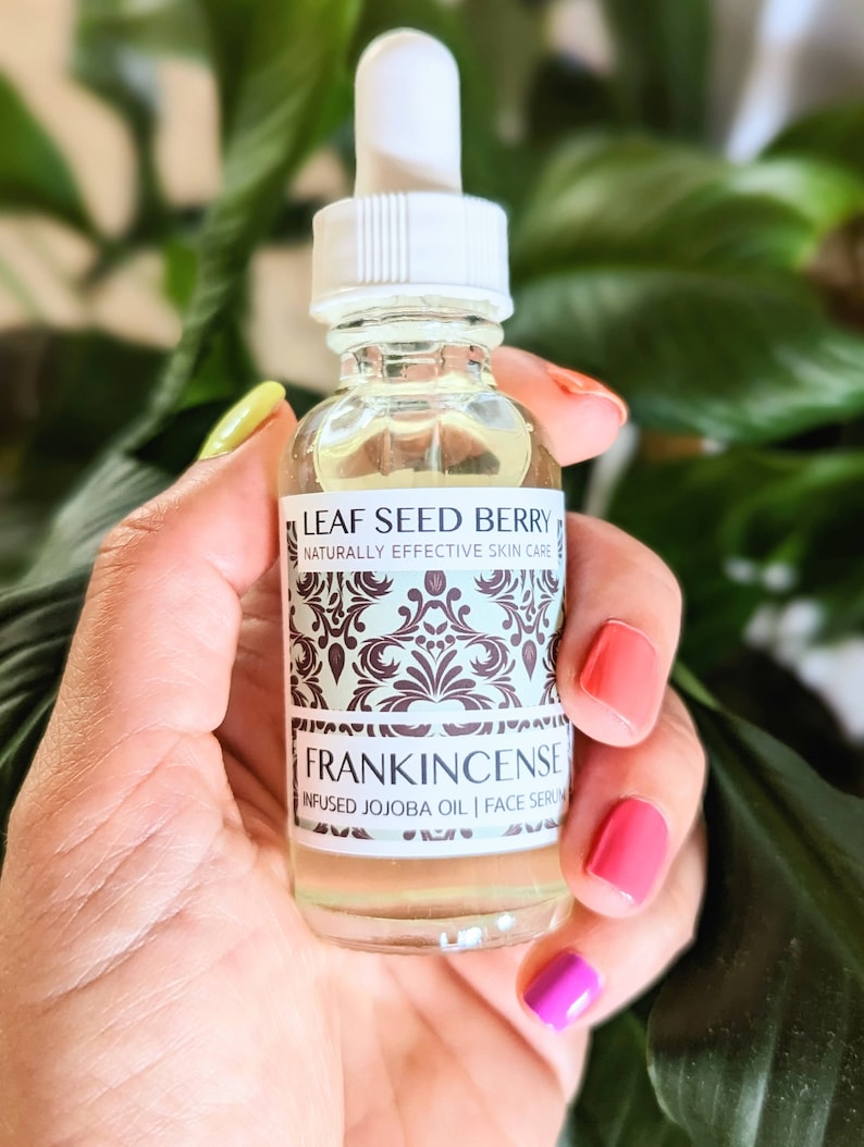 May include: A clear glass bottle with a white dropper top and a label that reads "Leaf Seed Berry Naturally Effective Skin Care Frankincense Infused Jojoba Oil | Face Serum"