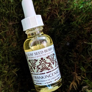 May include: A clear glass bottle with a white dropper top and a label that reads "Leaf Seed Berry Naturally Effective Skin Care Frankincense Infused Jojoba Oil | Face Serum".