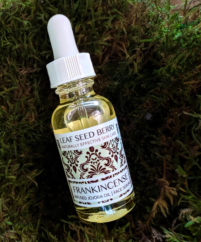 May include: A clear glass bottle with a white dropper top and a label that reads "Leaf Seed Berry Naturally Effective Skin Care Frankincense Infused Jojoba Oil | Face Serum".