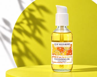 May include: A clear glass bottle with a white pump dispenser containing golden cleansing oil. The label features illustrations of citrus slices and the text Leaf Seed Berry Naturally Effective Skin Care Cleansing Oil Citrus Medley 2 fl oz.