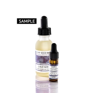 May include: Two glass bottles with dropper tops, one larger and one smaller. The larger bottle is clear and contains a light yellow liquid. The smaller bottle is amber colored and contains a darker liquid. Both bottles have labels with the text "LEAF SEED BE" and "LAVENDER USED JOJOBA OIL FAC". The smaller bottle also has the text "SAMPLE LAVENDER USED JOJOBA OIL" and "SEED BERRY SKIN".