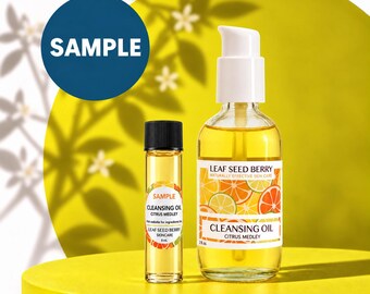 May include: A clear glass bottle of Leaf Seed Berry Cleansing Oil Citrus Medley with a white pump dispenser and a smaller matching sample vial with a black cap. Both containers feature labels with citrus fruit graphics and text.