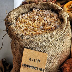 May include: A burlap sack filled with frankincense resin. The sack has a brown paper tag with the word "Frankincense" written in English and Hebrew.