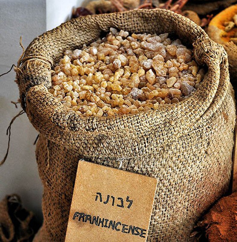 May include: A burlap sack filled with frankincense resin. The sack has a brown paper tag with the word "Frankincense" written in English and Hebrew.