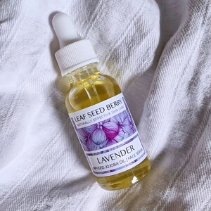 May include: A clear glass bottle with a dropper top filled with a yellow liquid. The bottle is labeled "LEAF SEED BERRY NATURALLY EFFECTIVE SKIN CARE LAVENDER INFUSED JOJOBA OIL | FACE SERUM".