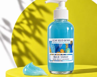 Może przedstawiać: Przezroczysta szklana butelka żelu myjącego Blue Tansy Milk Jelly Cleanser z białą pompką. Etykieta zawiera napis Leaf Seed Berry, Naturally Effective Skin Care, Blue Tansy Milk Jelly Cleanser, 6 fl. oz. Obok znajduje się kropla niebieskiego żelu.