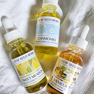May include: Three glass bottles of face serum with dropper tops. The bottles are labeled with the brand name "Leaf Seed Berry" and the scents "Chamomile", "Sweet Meadow", and "Vanilla Bean".