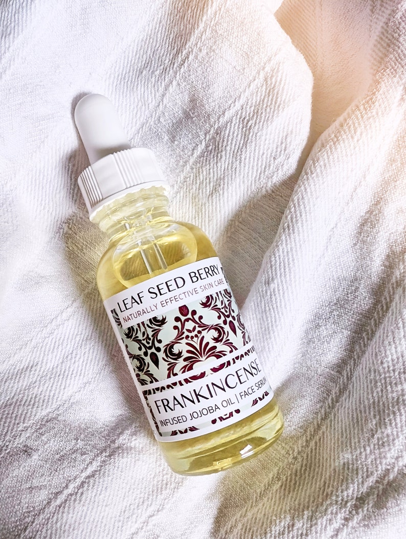 May include: A clear glass bottle with a white dropper top and a yellow liquid inside. The label is white with black text that reads "LEAF SEED BERRY NATURALLY EFFECTIVE SKIN CARE FRANKINCENSE INFUSED JOJOBA OIL | FACE SERUM".