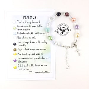 Puede incluir: Un brazalete de plata con un dije de cruz y cuentas de colores. El brazalete viene acompañado de una tarjeta con el texto del Salmo 23, un pasaje de la Biblia.