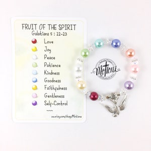 May include: A colourful beaded bracelet with a silver dove charm. The bracelet is made with pastel-coloured beads and clear crystals. The card attached to the bracelet lists the "Fruit of the Spirit" from Galatians 5:22-23, with each bead representing a different fruit: love, joy, peace, patience, kindness, goodness, faithfulness, gentleness, and self-control.