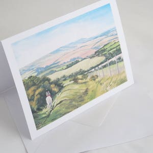 Peut inclure: Une carte blanche avec une peinture colorée d'une personne à cheval sur un chemin à travers un champ vert. L'arrière-plan montre un paysage vallonné avec des collines et des vallées.
