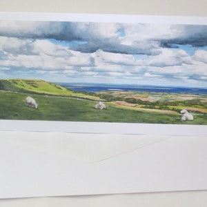 Puede incluir: Una pintura de acuarela de un paisaje rural con colinas onduladas, un cuerpo de agua distante y un cielo nublado. Tres ovejas blancas pastan en un campo en primer plano.