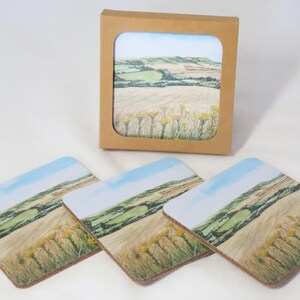 Può includere: Set di quattro sottobicchieri quadrati con un dipinto di paesaggio di colline, campi e cielo blu. I sottobicchieri sono esposti con un sottobicchiere abbinato in una scatola di cartone marrone. L'opera d'arte include fiori selvatici gialli.